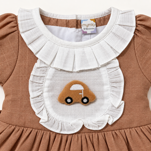 Close-up of car applique and white ruffled bib on brown baby dress