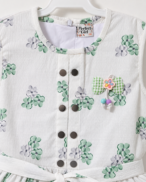 Close-up of Inaabia white and mint floral dress showing dark buttons and decorative brooch