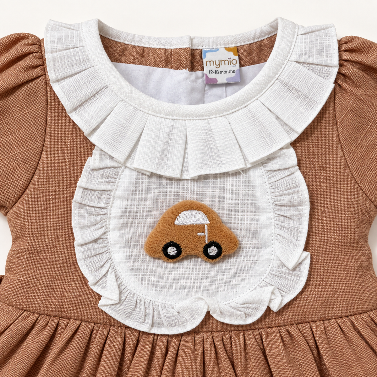 Close-up of car applique and white ruffled bib on brown baby dress